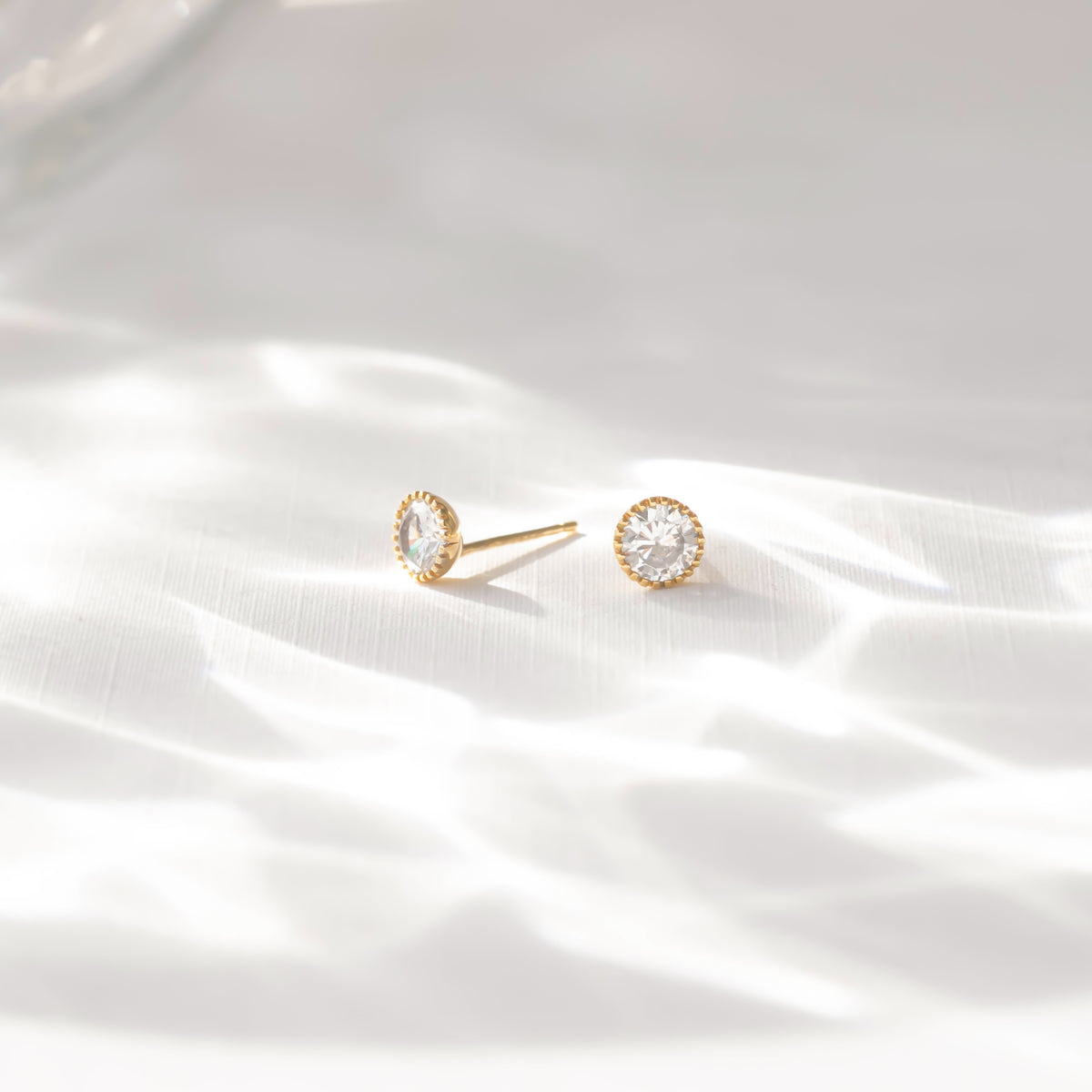 Gold stud earrings on a white satin background