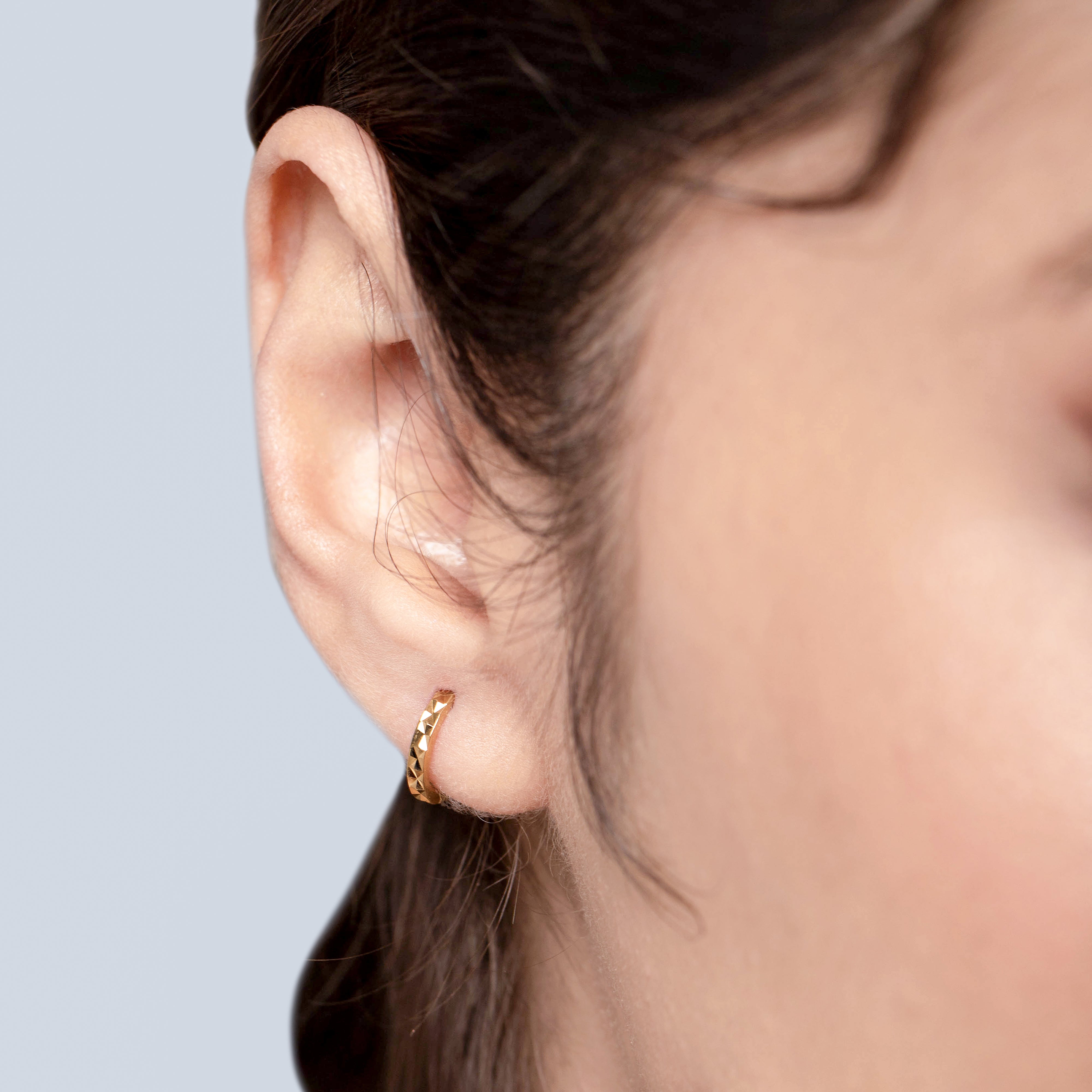 Close-up of a person wearing a gold hoop earring against a neutral background