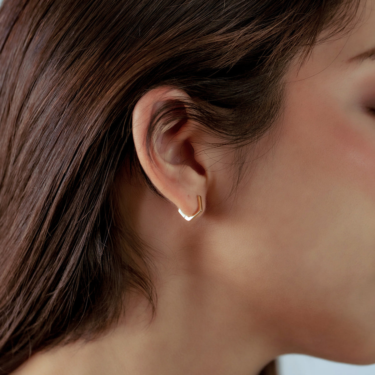Close-up of an ear wearing a gold earring with hair partially covering the face.