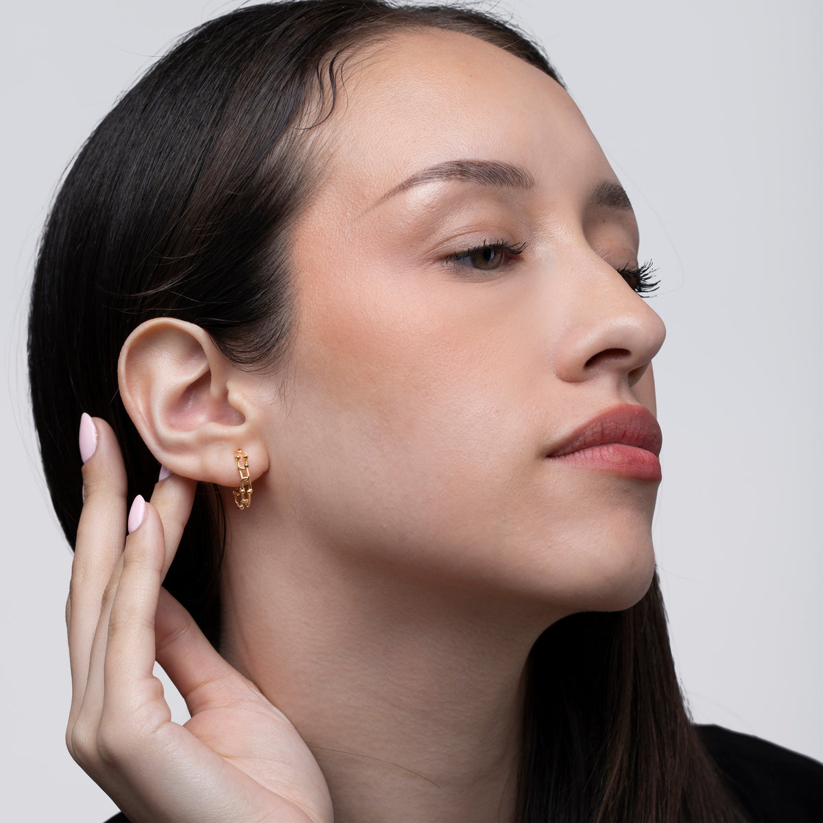 Gold-tone chain link huggie earring worn on the ear in a close-up portrait