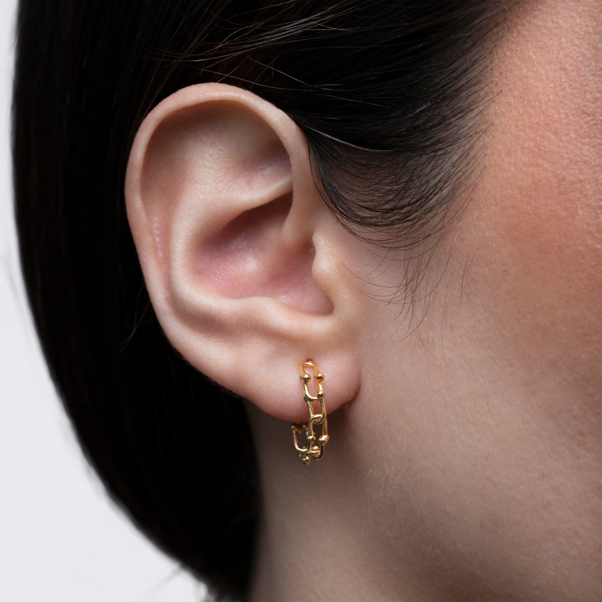Gold-tone chain link huggie earring worn on the ear in a side close-up view