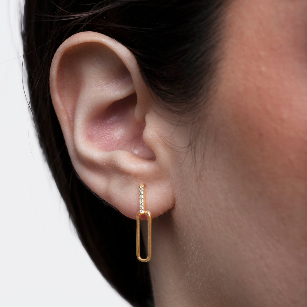 Gold-tone rectangular drop earring with clear stones worn in a close-up ear view