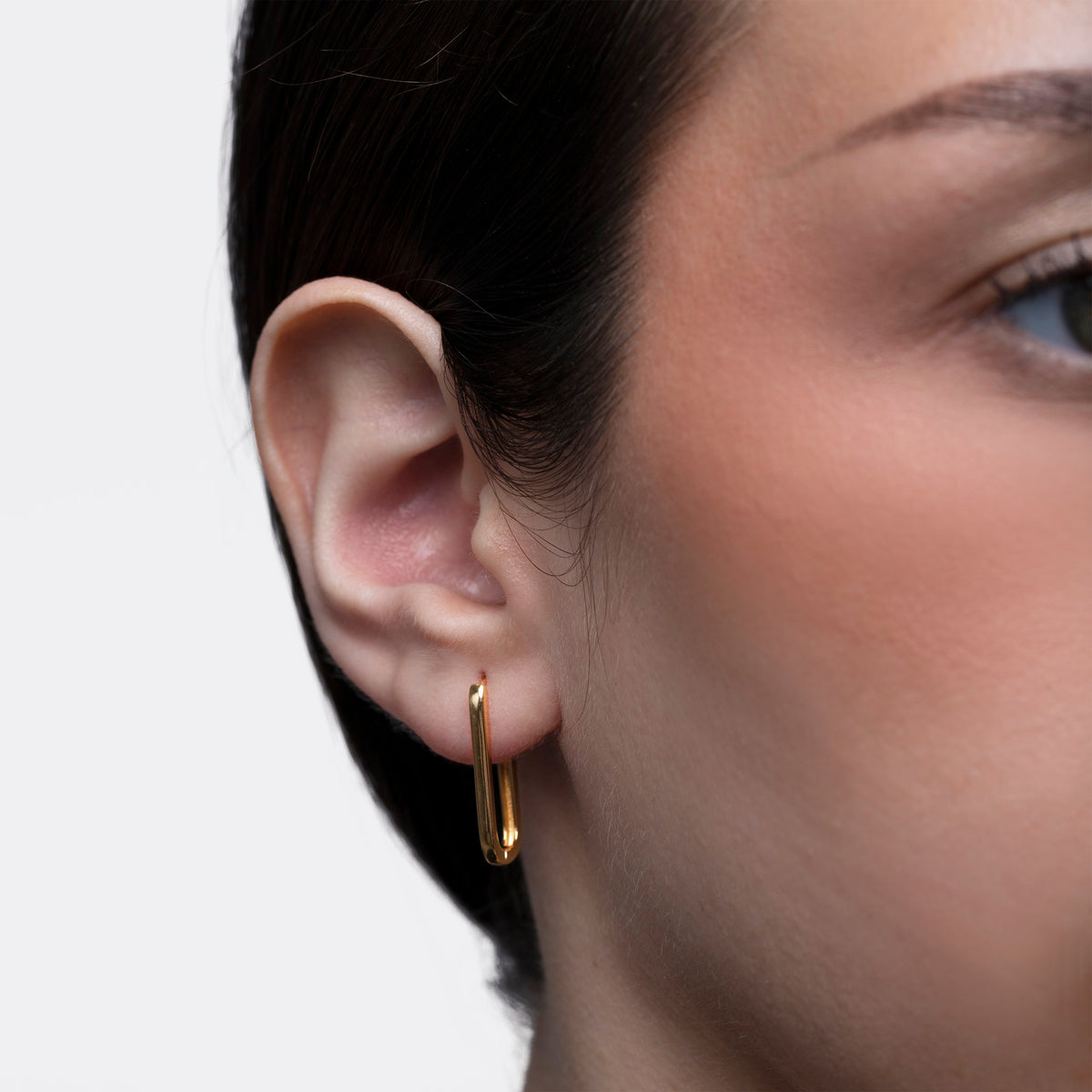Close-up of a person wearing a gold hoop earring with a neutral background