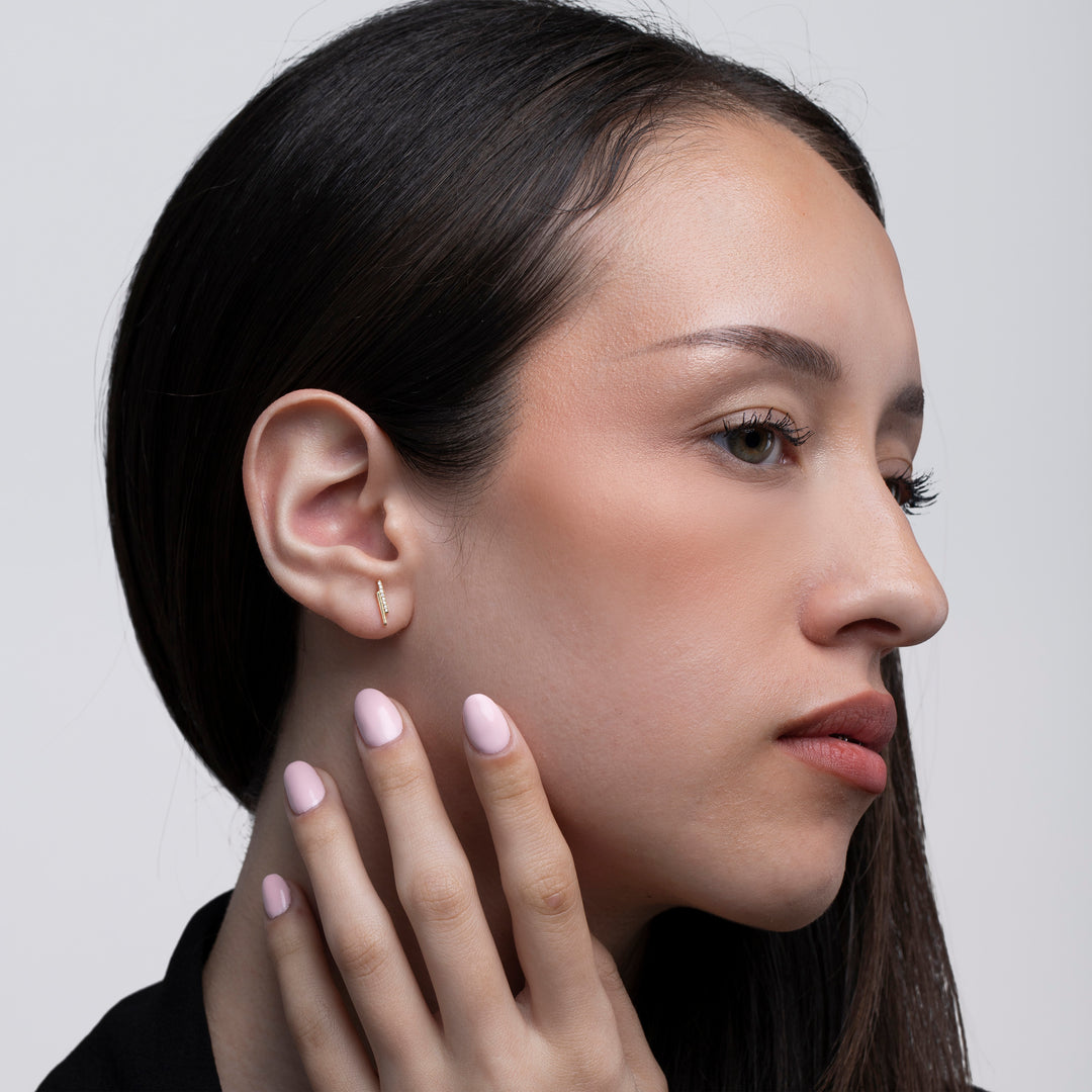 Model touching her face wearing gold studs with crystals against a neutral background