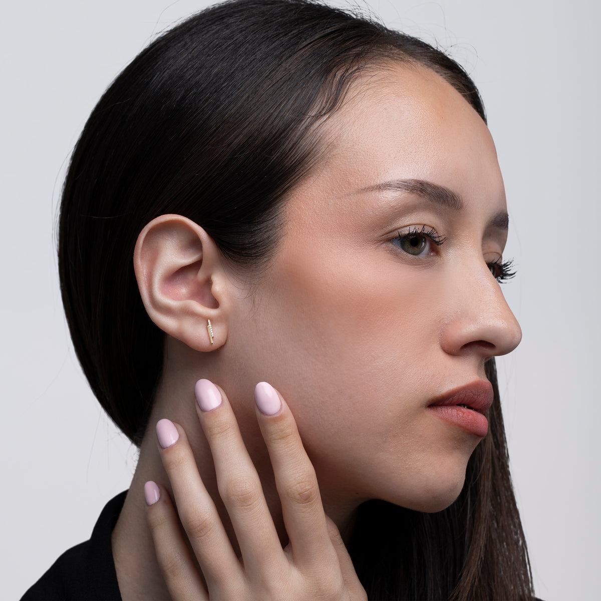 Model touching her face wearing gold studs with crystals against a neutral background