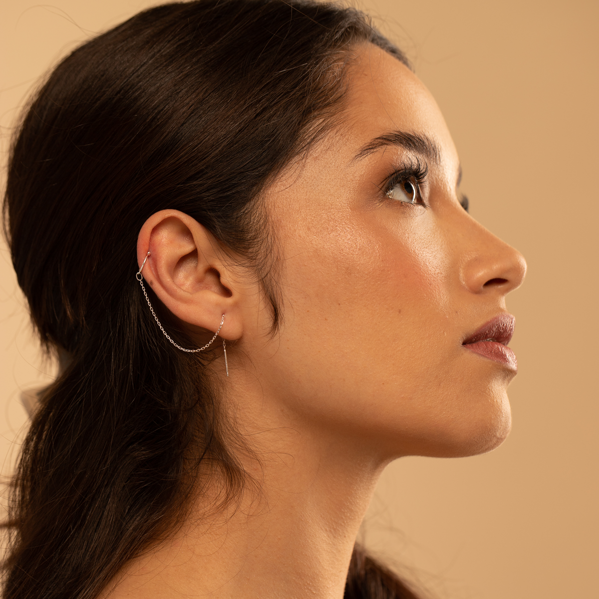 Side profile of a woman with dark hair and silver earrings against a beige background