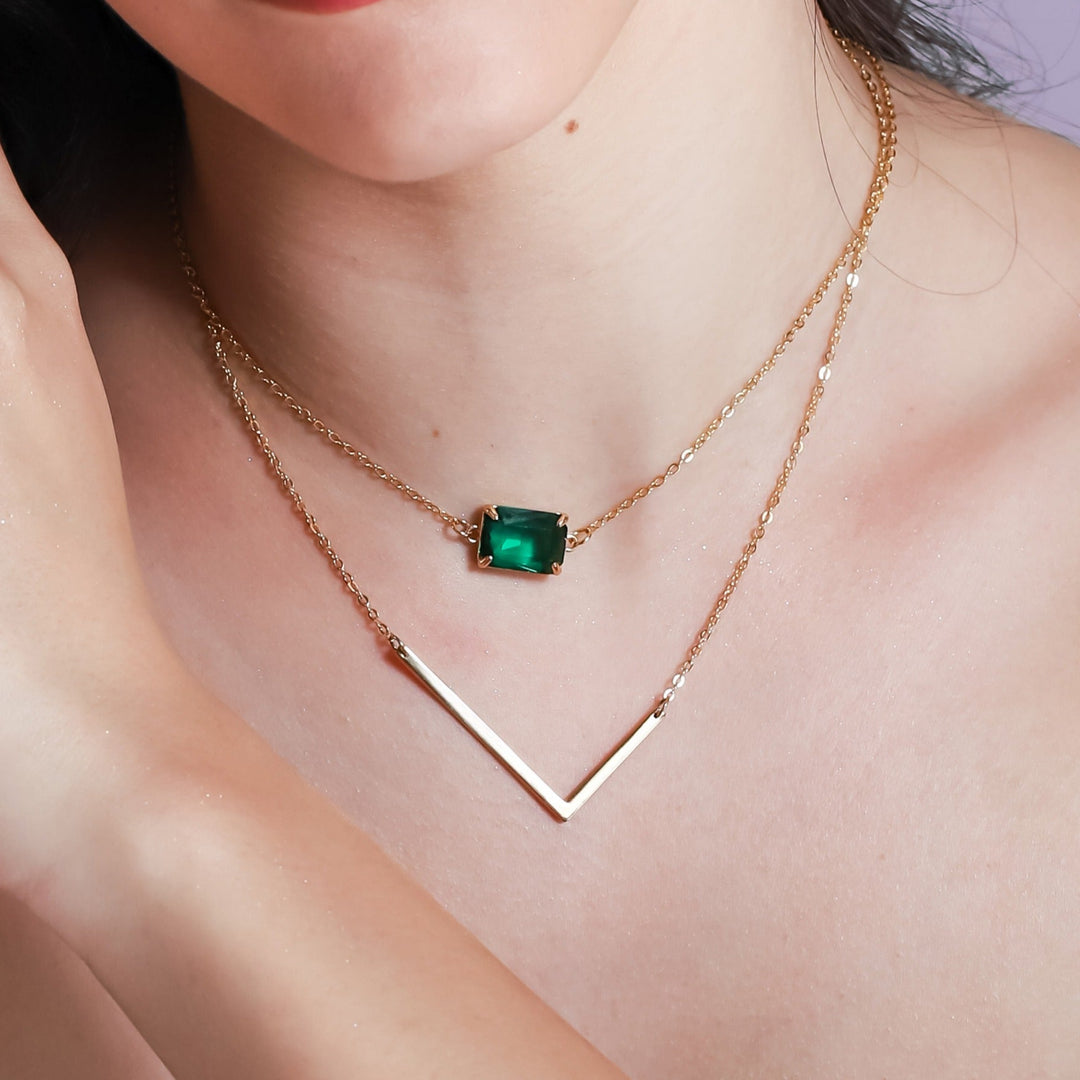 Close-up of a woman wearing a gold necklace with an emerald pendant.