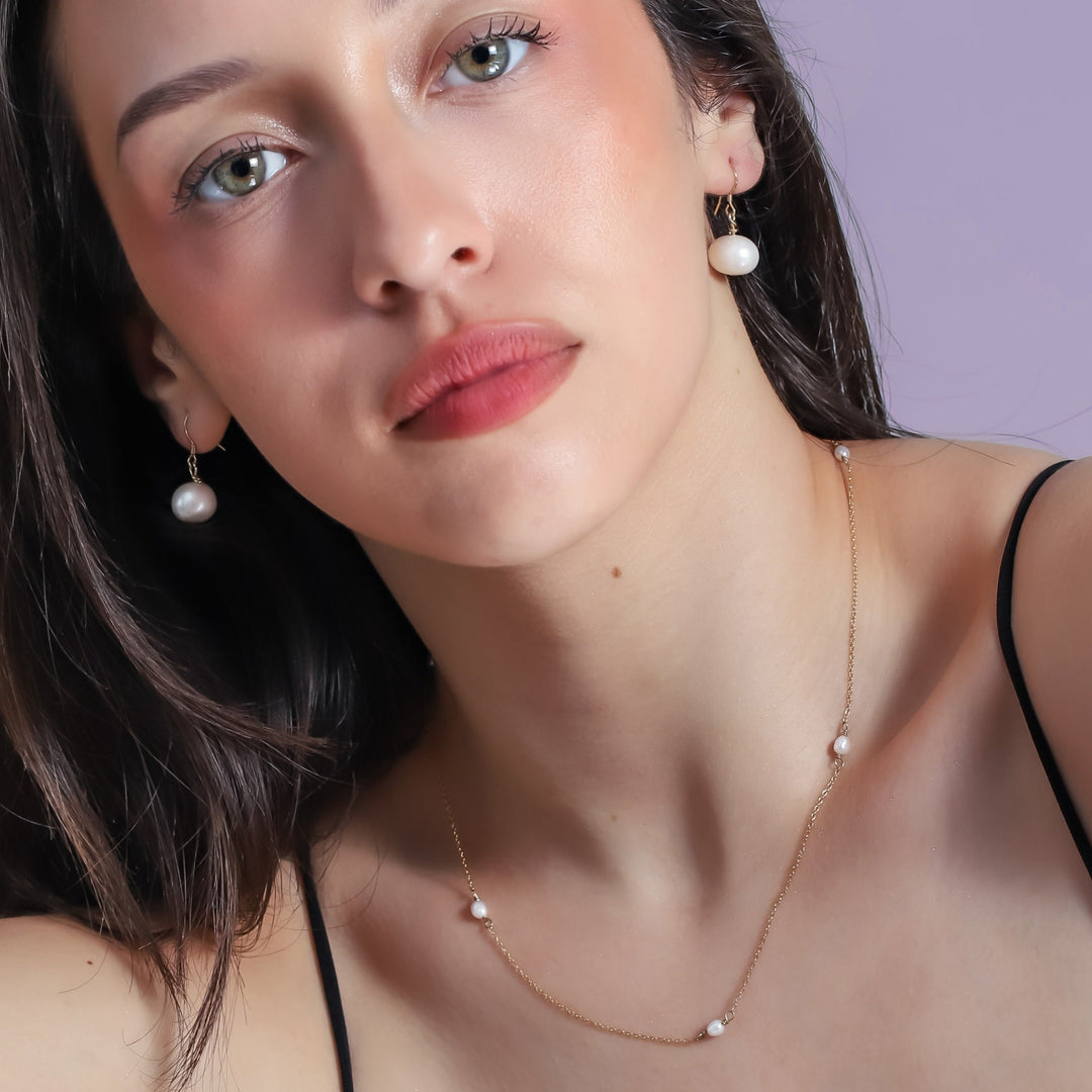 Woman wearing pearl earrings and necklace against a light purple background