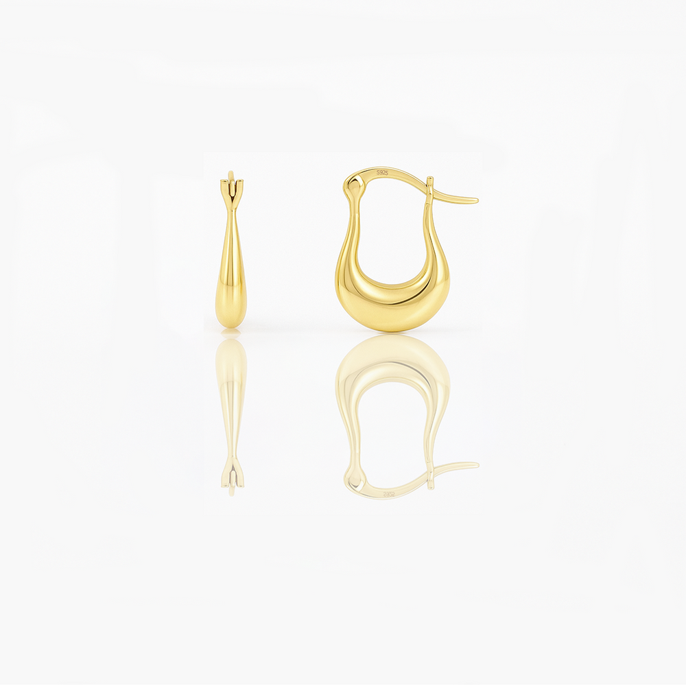 A pair of gold vermeil huggie earrings on a white background, reflecting light on their surface.