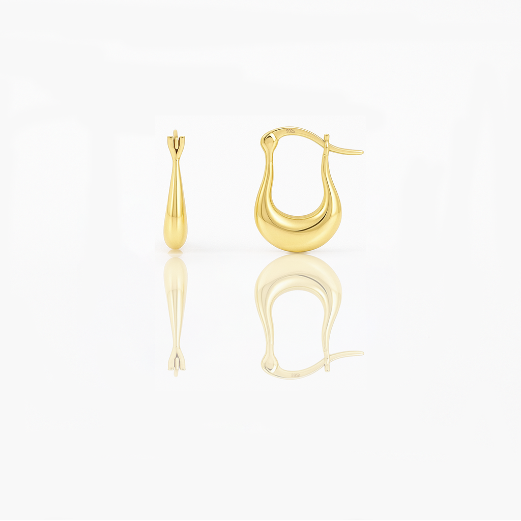 A pair of gold vermeil huggie earrings on a white background, reflecting light on their surface.