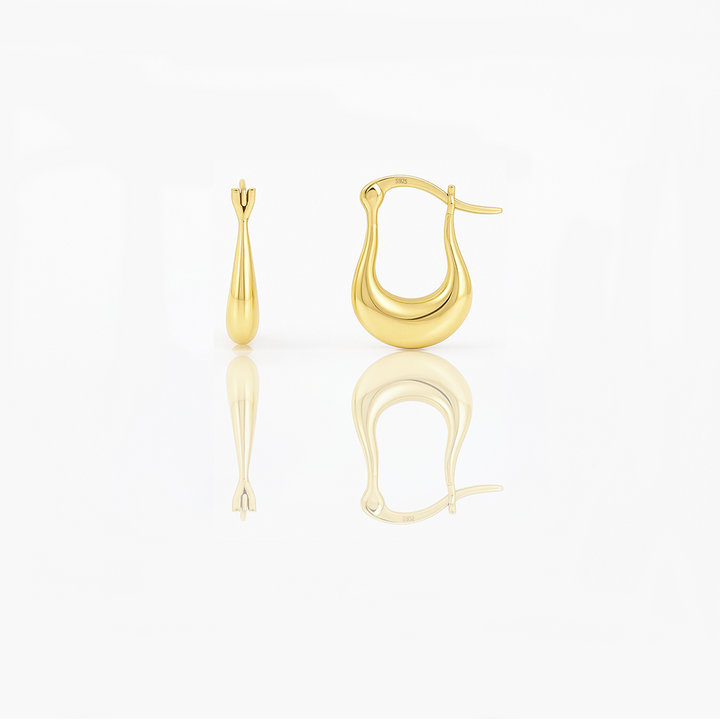 A pair of gold vermeil huggie earrings on a white background, reflecting light on their surface.
