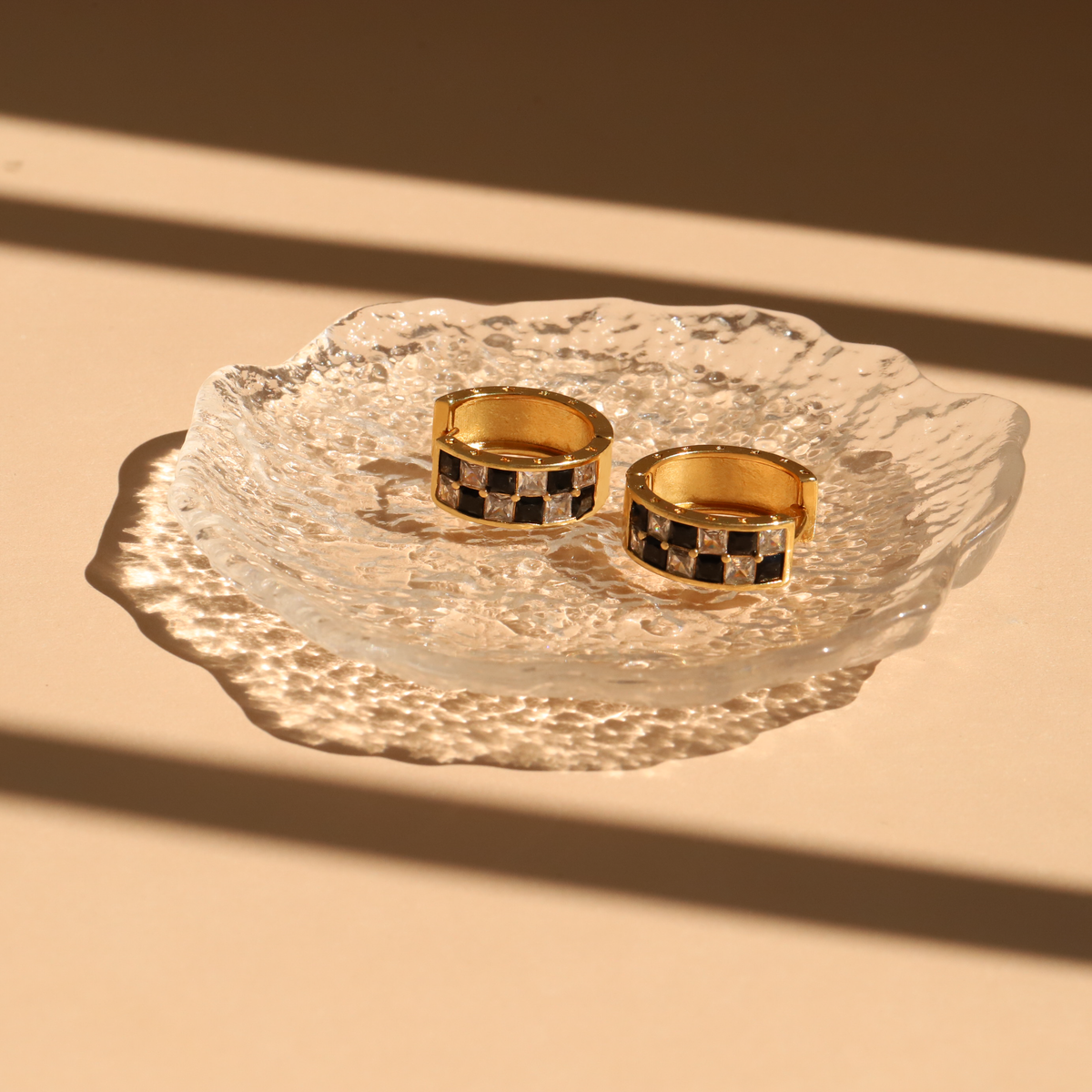 Two gold rings with a black and white pattern on a textured glass dish against a beige background