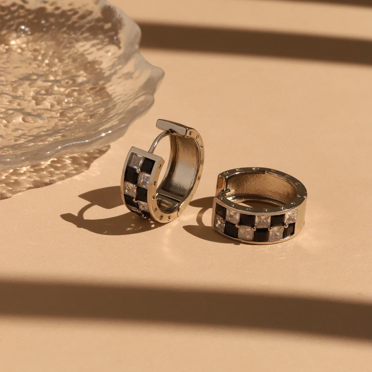 Silver hoop earrings with a black and white checkered pattern on a beige surface