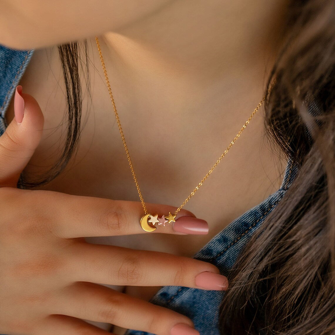 Gold-tone necklace with crescent moon and star charms worn at the neckline with a hand nearby
