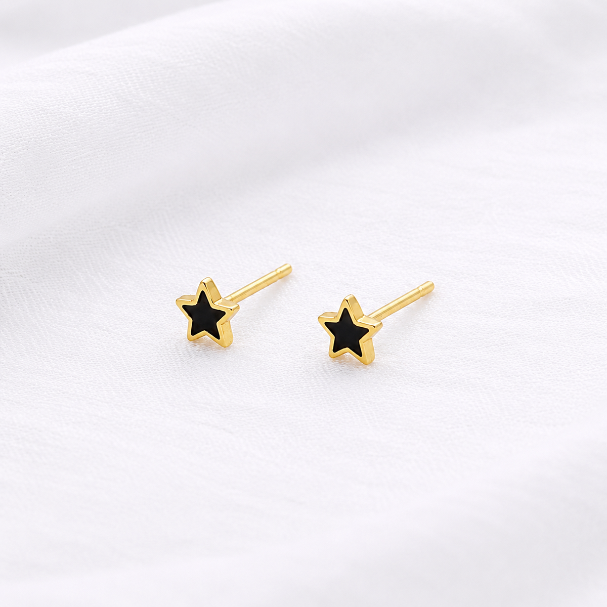 Gold-tone star stud earrings with black centers displayed on softly textured white fabric