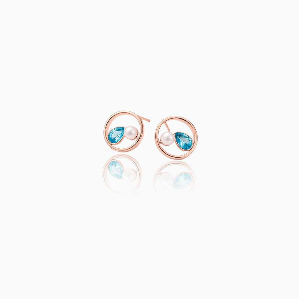 Pair of rose gold earrings with blue gemstones and pearls on a white background