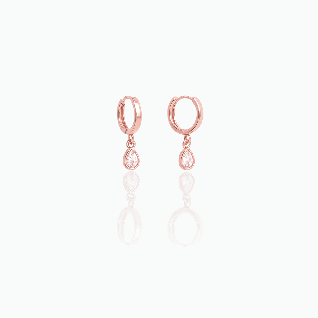 Rose-gold-tone dangle huggie hoop earrings with clear teardrop stones on a white background