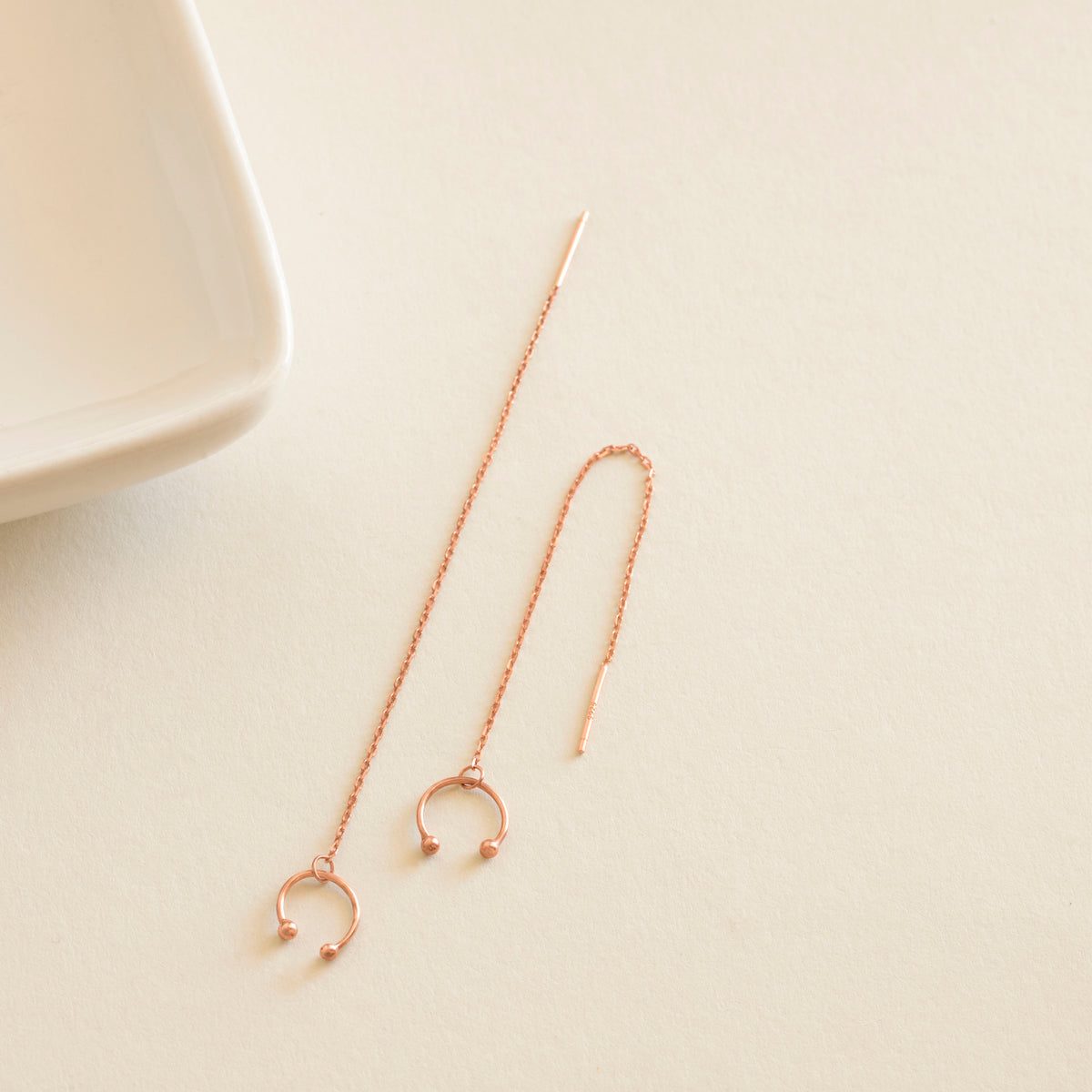Rose gold earrings on a light beige surface with a white dish in the background