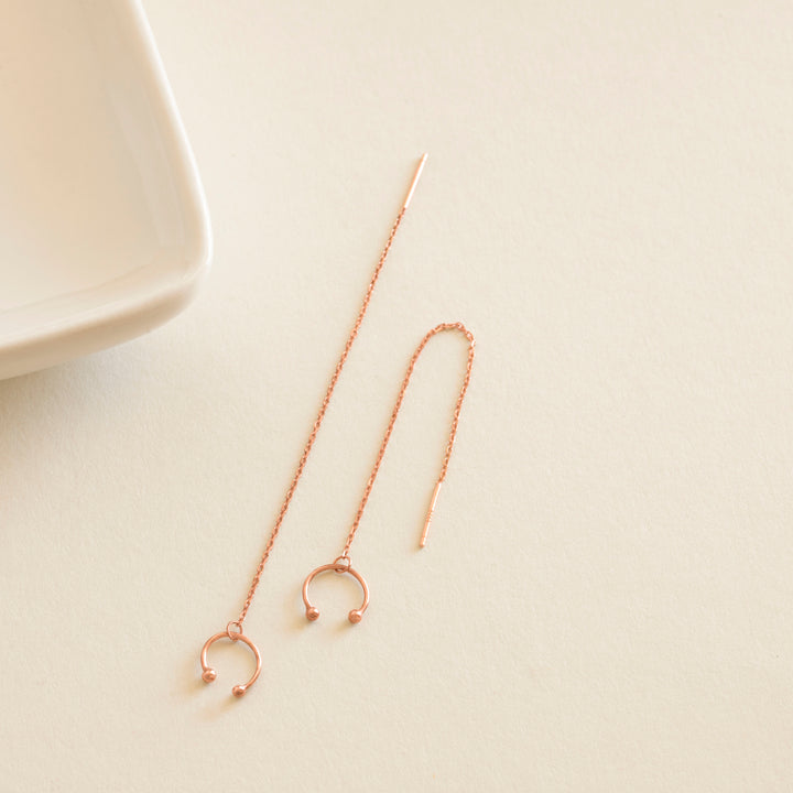 Rose gold earrings on a light beige surface with a white dish in the background