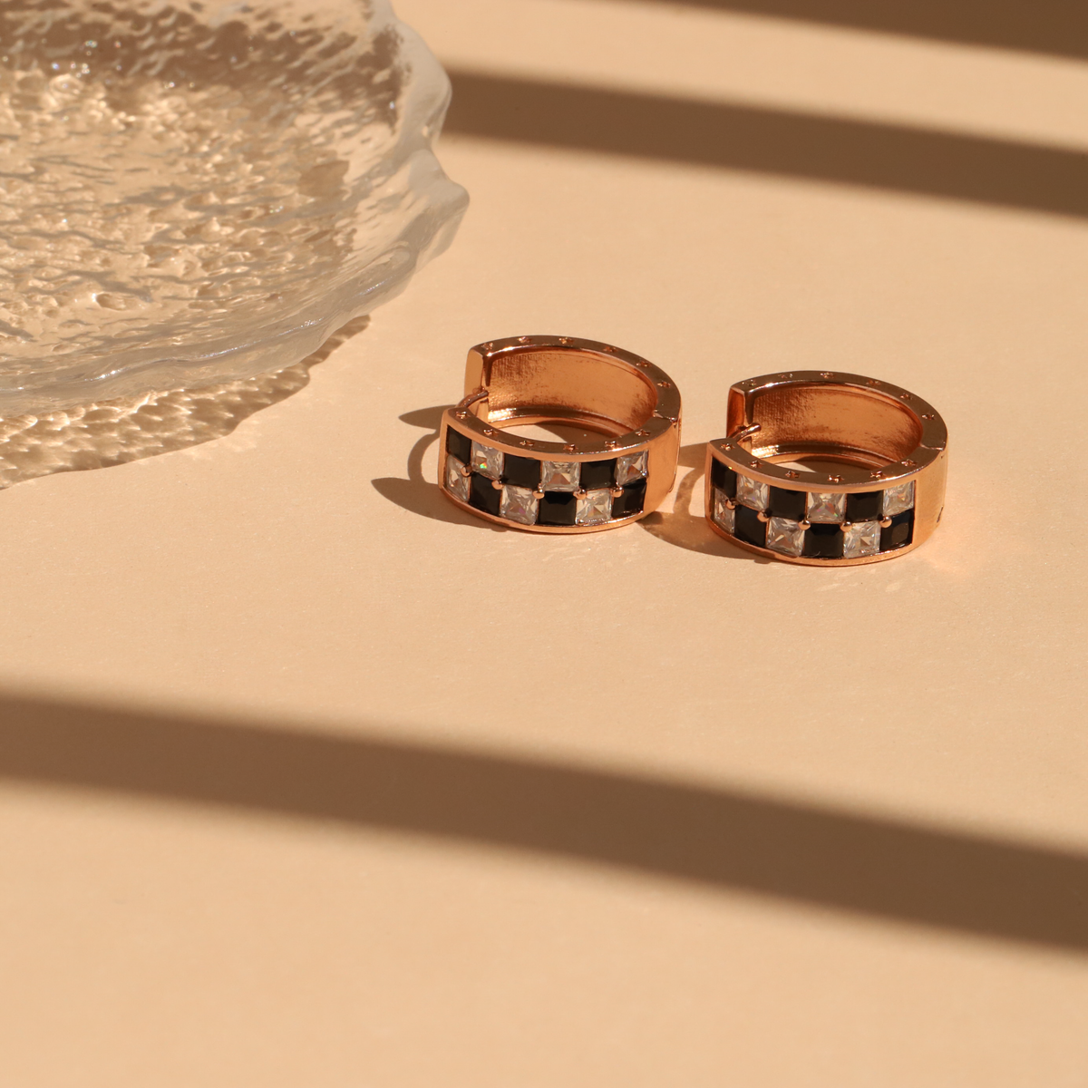 Rose gold hoop earrings with black and white checkered pattern on a beige surface.