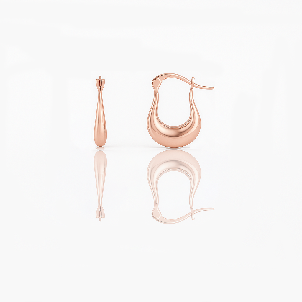 A pair of rose gold vermeil huggie earrings on a white background, reflecting light on their surface.