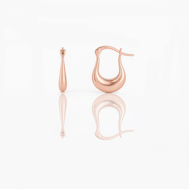 A pair of rose gold vermeil huggie earrings on a white background, reflecting light on their surface.