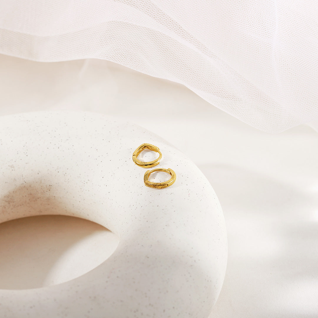 Gold-tone huggie hoop earrings displayed on a speckled white surface with sheer fabric