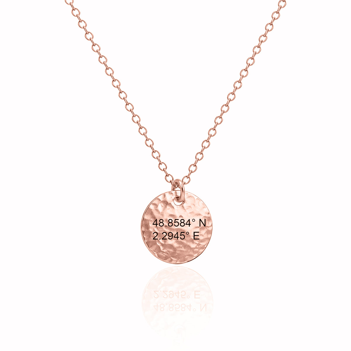 Rose-gold-tone hammered round disc necklace engraved 48.8584° N, 2.2945° E on a white background