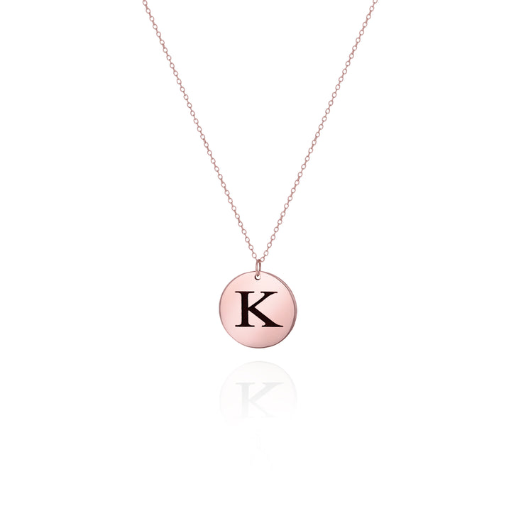 A rose gold-colored disc necklace with the initial 'K' engraved on the charm, displayed against a white background.