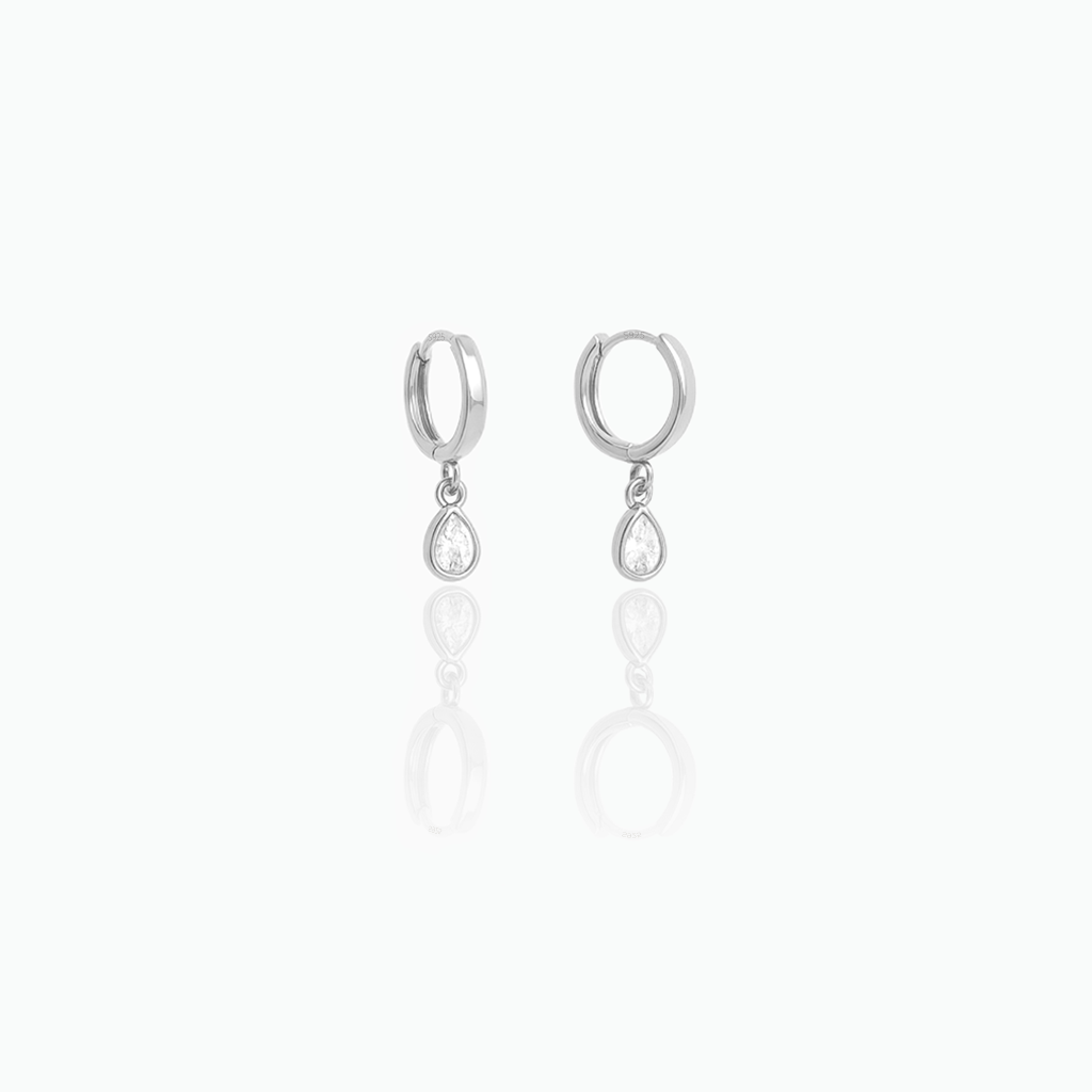 Silver-tone dangle huggie hoop earrings with clear teardrop stones on a white background