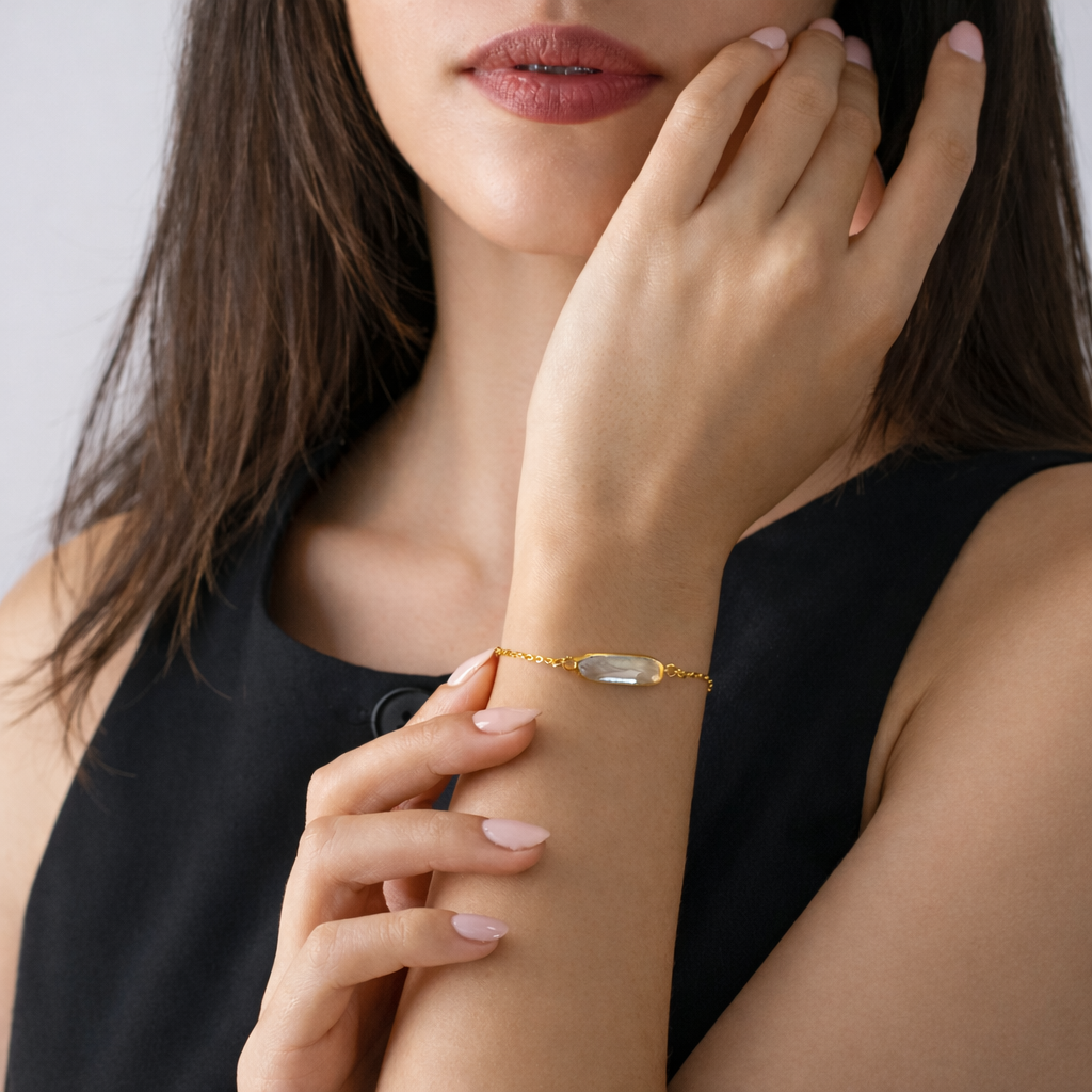 Woman wearing a delicate bracelet with a clear rectangular stone, hand resting near her face