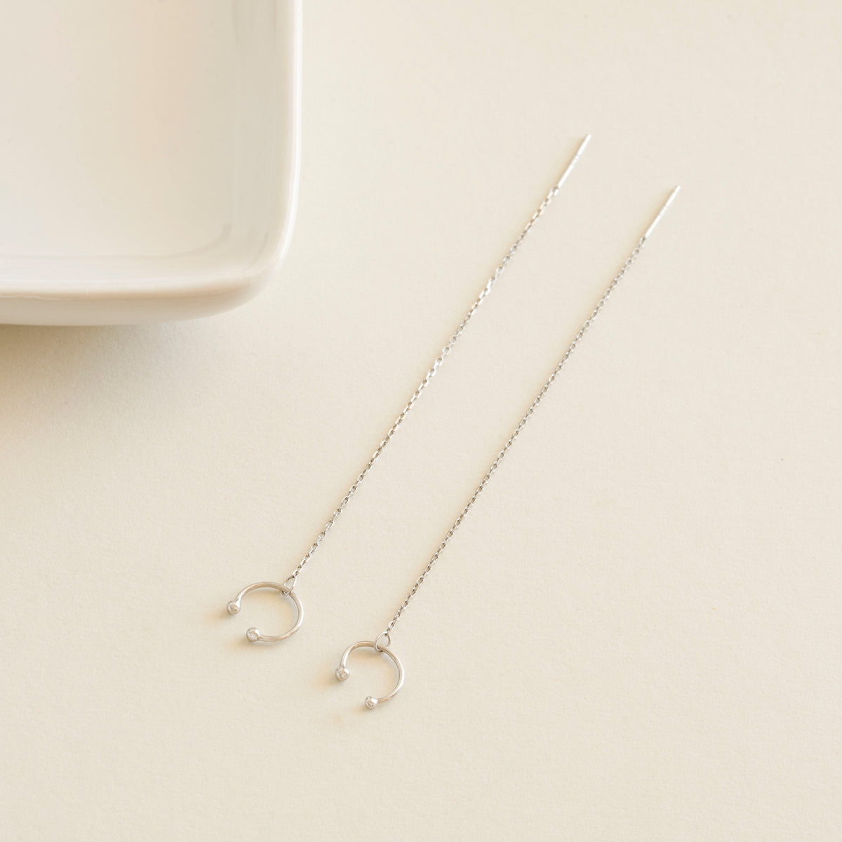Silver chain earrings cuff on a beige surface