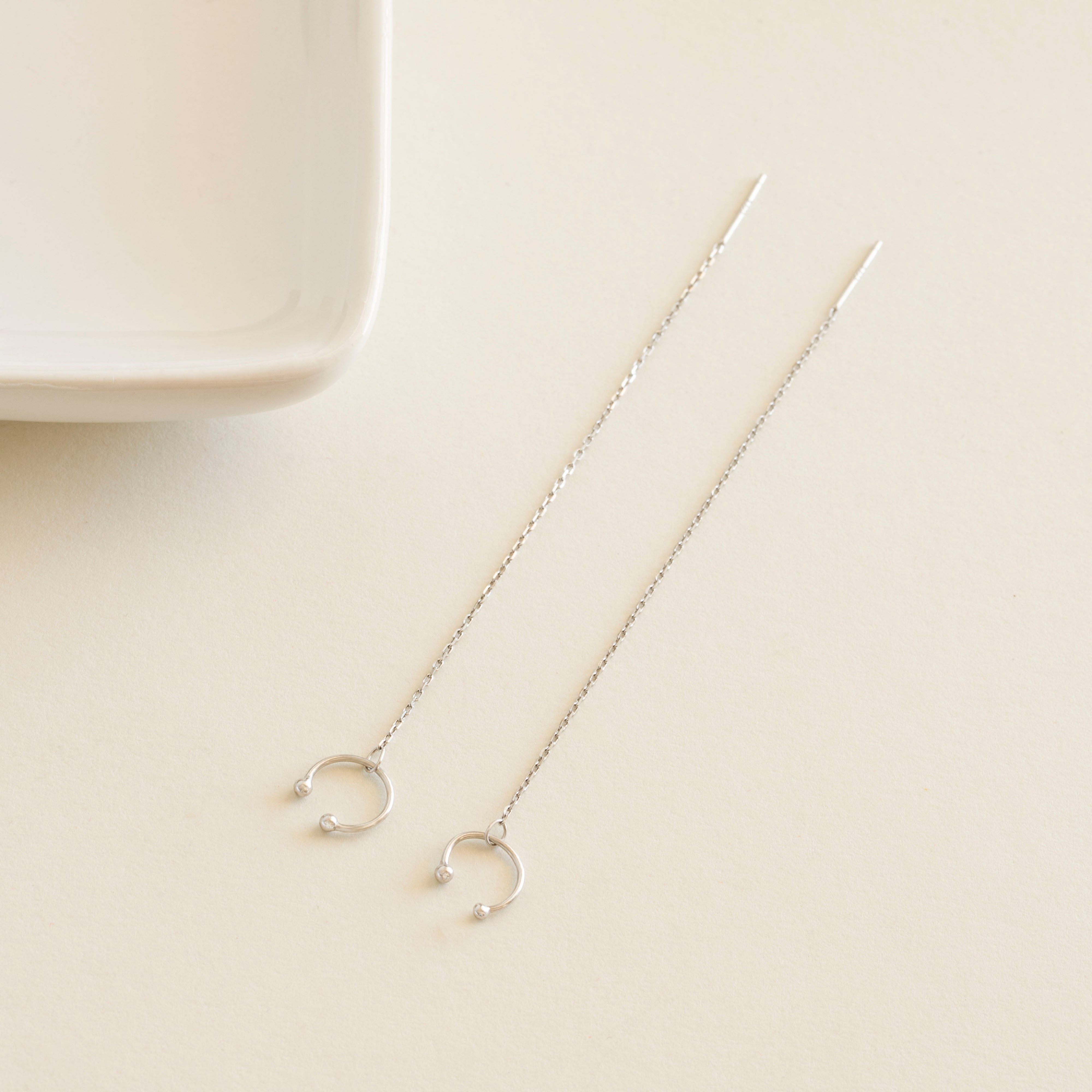 Silver chain earrings cuff on a beige surface