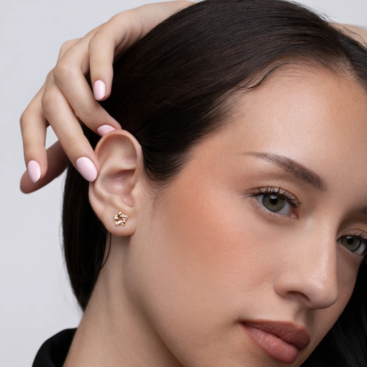 Close-up of a woman wearing a gold earring with a neutral background