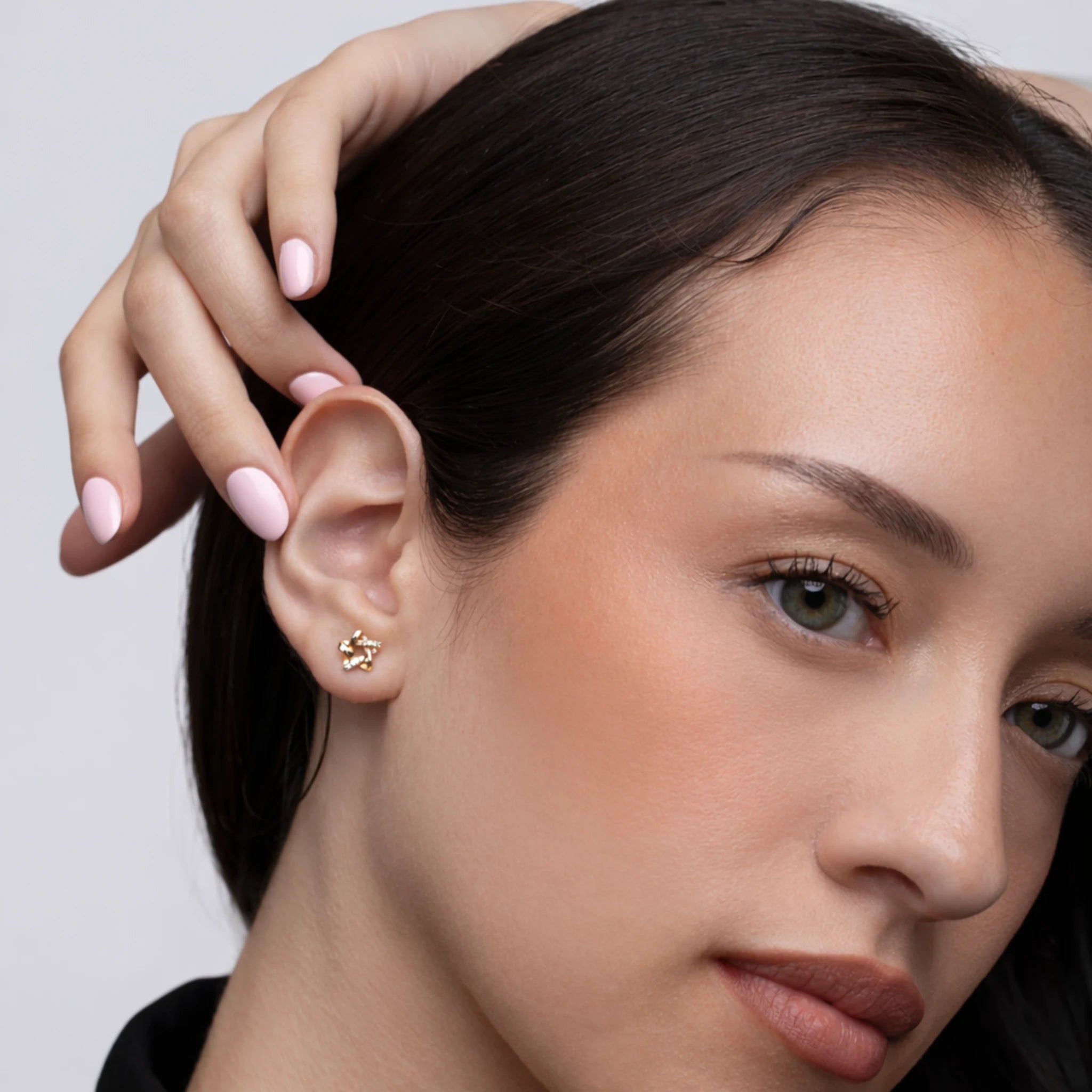 Close-up of a woman wearing a gold earring with a neutral background