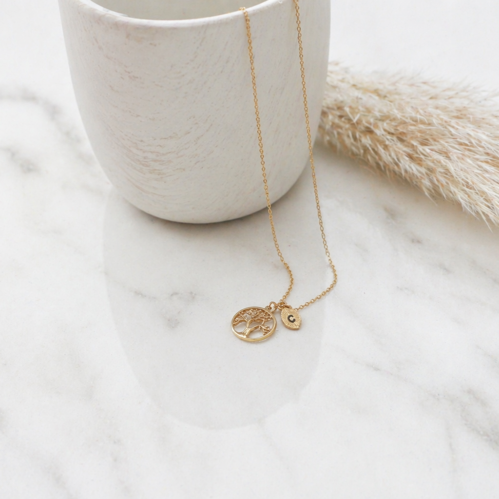 Gold-tone tree of life necklace with two leaf-shaped initial charms engraved C and V on a white background