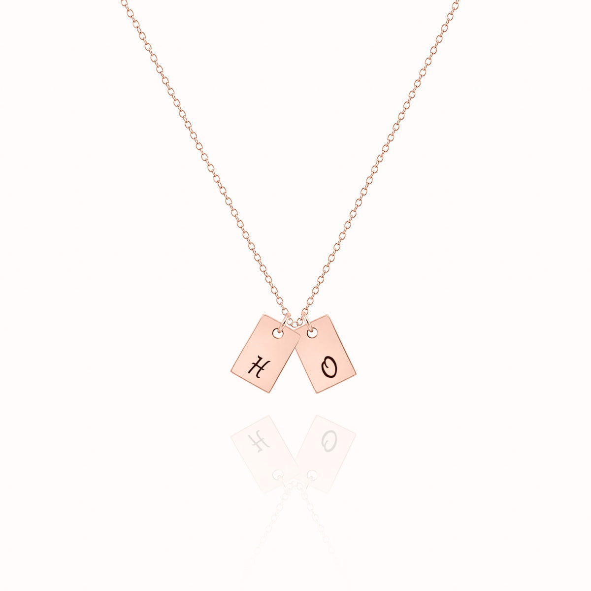 Rose-gold-tone necklace with two rectangular tag pendants engraved with letters on a white background