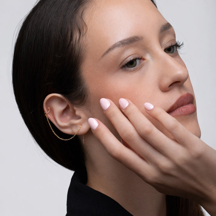 Close-up of a woman's face with hand near her face, wearing a gold chain cuff earring.