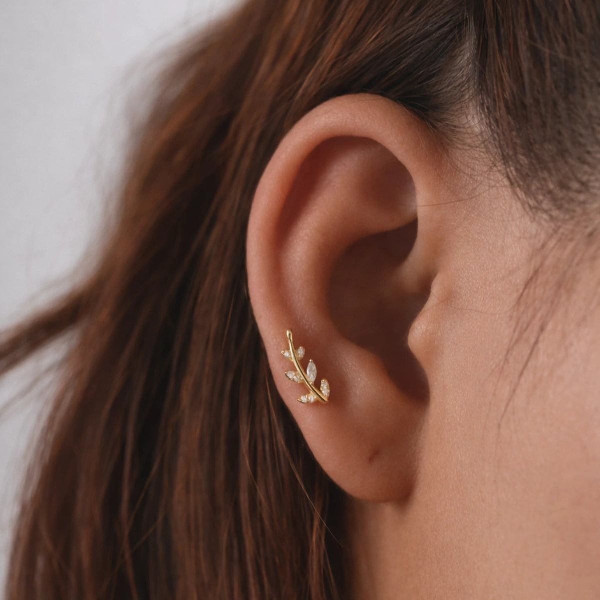 Close-up of an ear wearing a gold earring with a blurred background
