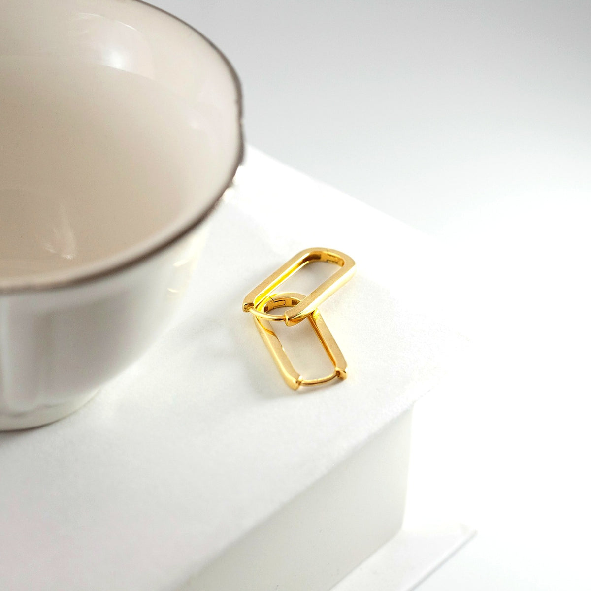 Gold hoops on a white surface next to a white mug