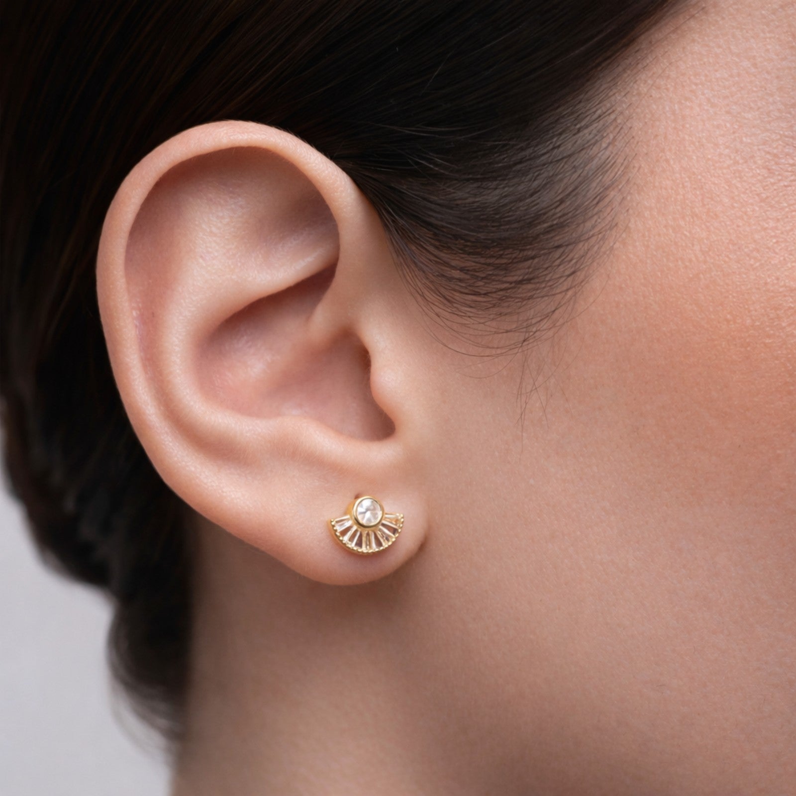 Gold earring worn on a person's ear with a neutral background