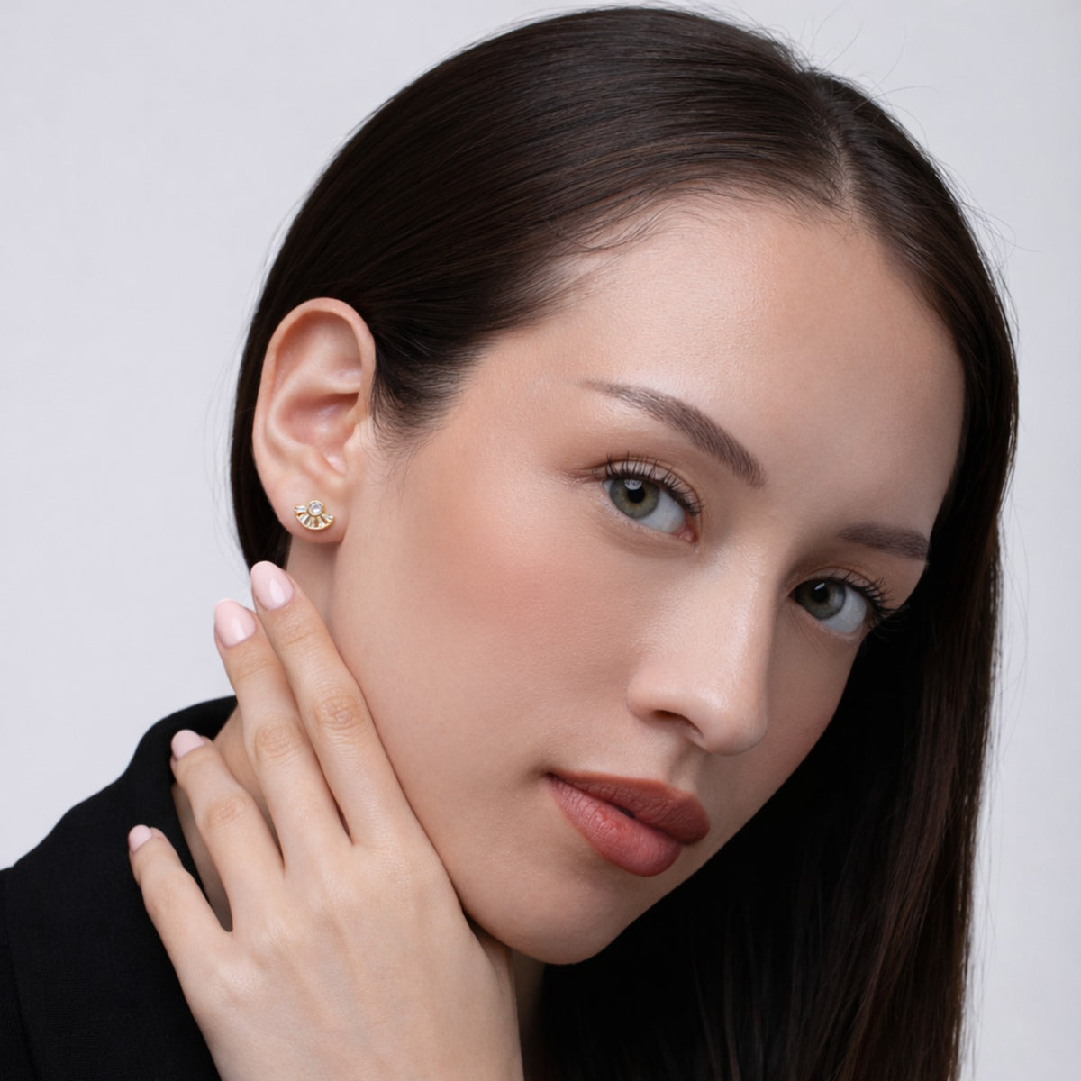 Close-up of a woman wearing a gold earring against a neutral background
