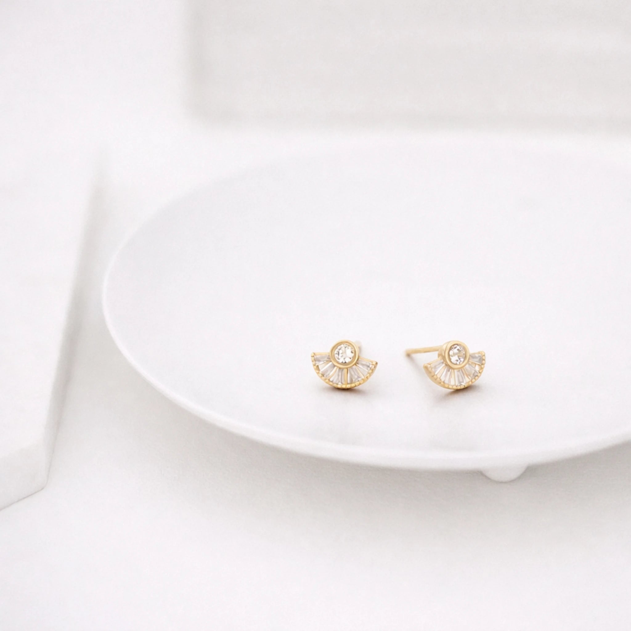 Gold earrings on a white dish with a white background