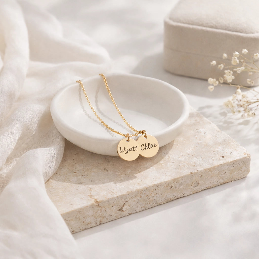 Gold-tone necklace with two round disc pendants engraved Wyatt and Chloe displayed on a white dish