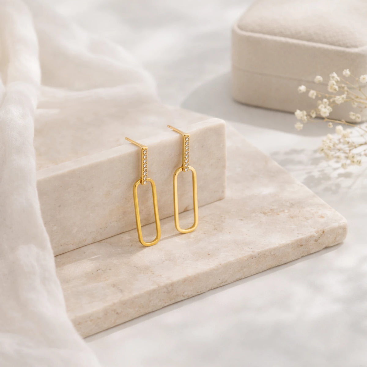 Gold-tone rectangular drop earrings with clear stones displayed on a pale stone surface