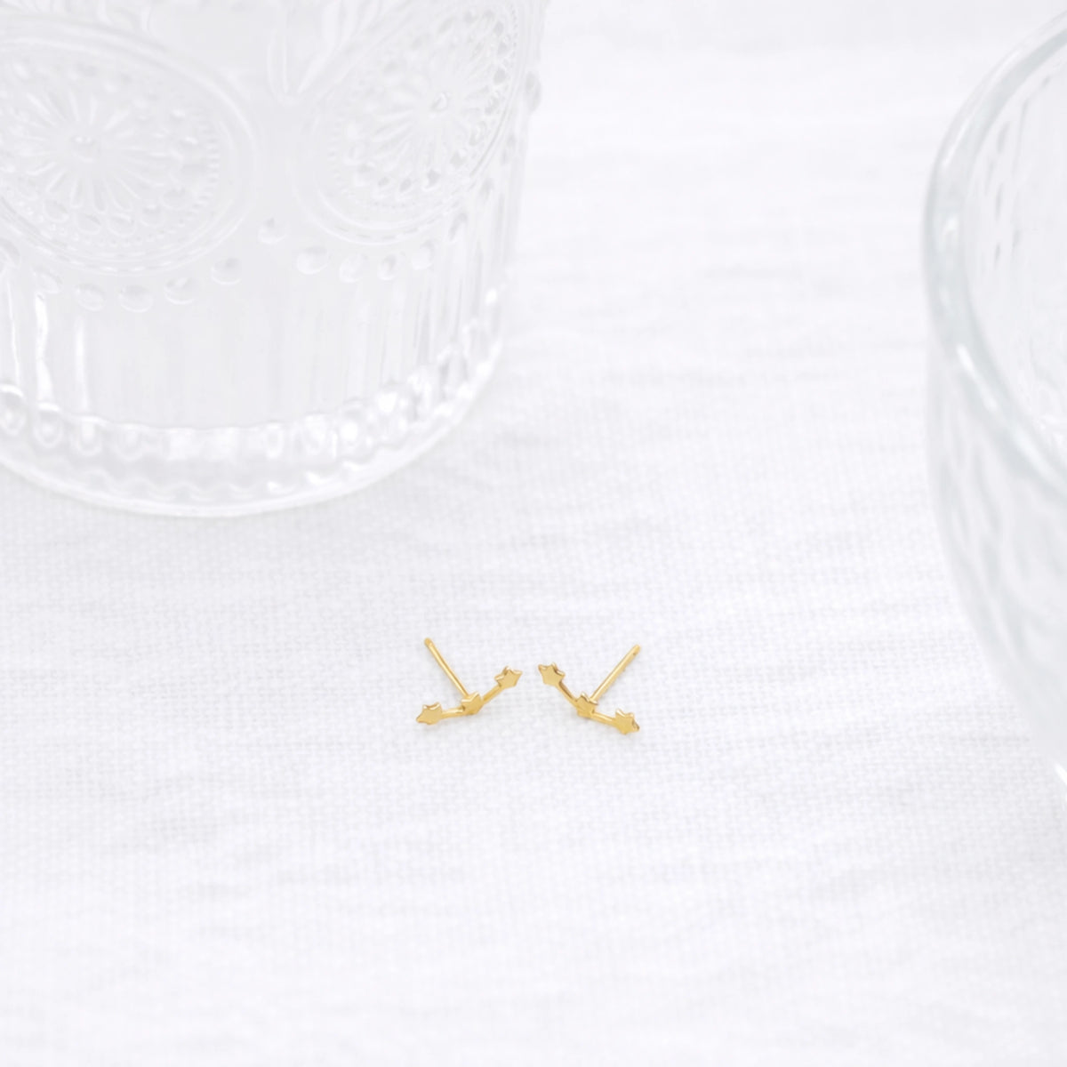 Gold-tone star constellation stud earrings displayed on white fabric