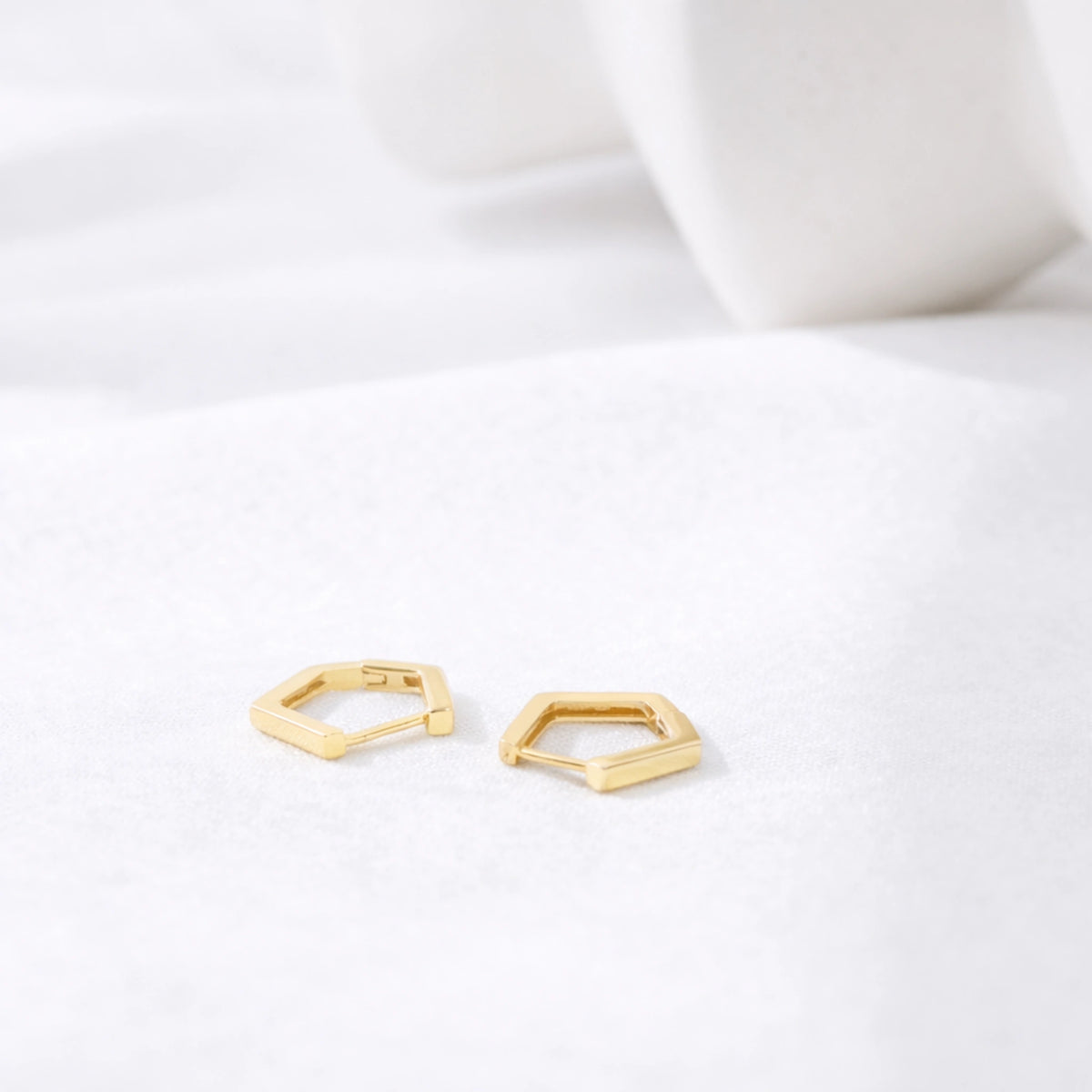 Gold-tone geometric huggie hoop earrings displayed on a white fabric surface