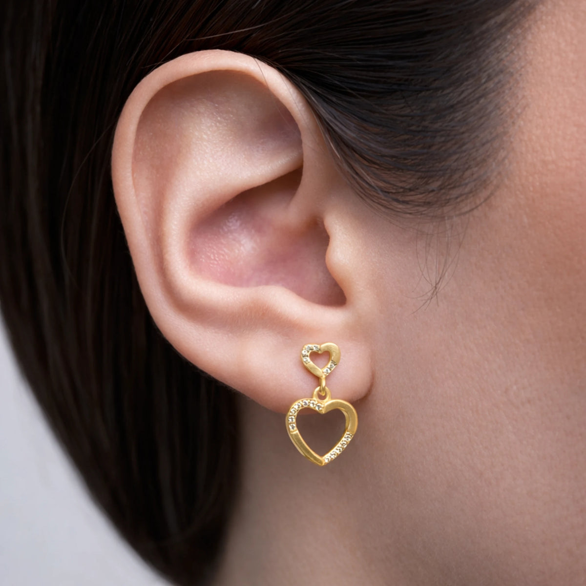 Gold heart-shaped earring worn on an ear with a neutral background