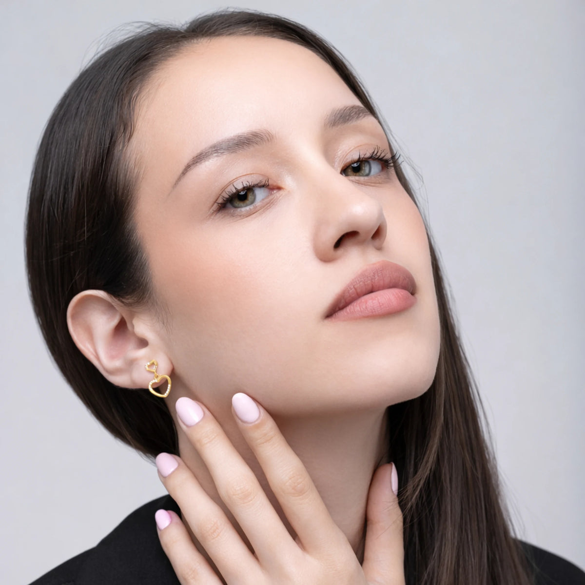 A woman wearing a heart-shaped gold earring with a plain background