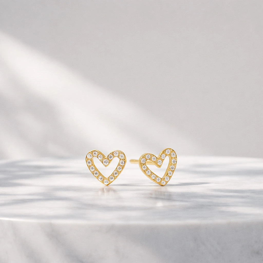 Gold-tone open heart stud earrings with clear stones displayed on a reflective white surface